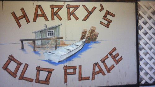 A painted sign reading "Harry's Old Place" with a boat, dock, and logs on a water background.