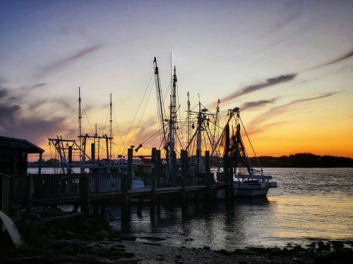 Fishing boats docked at a pier during sunset, with colorful clouds reflecting in the water.