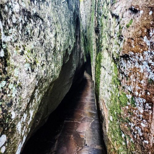 Narrow passage between two large, moss-covered rock formations, with a stone path leading through.