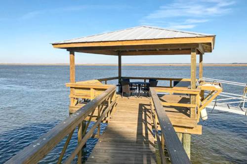 A wooden dock with a gazebo overlooking calm water and a clear blue sky.