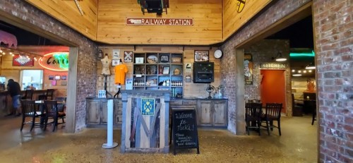Interior of a rustic bar with wooden decor, a welcome sign, and various memorabilia on display.