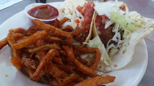 A plate featuring a taco with toppings and a side of crispy sweet potato fries, accompanied by a small cup of salsa.