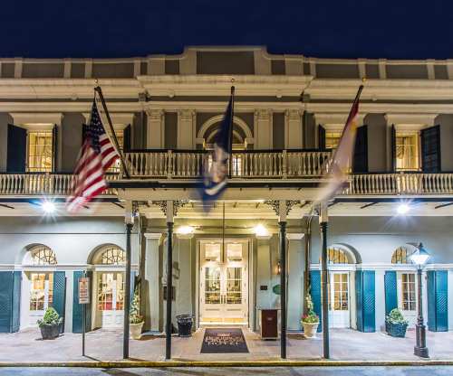 Historic hotel entrance at night, featuring flags and elegant architecture with lit windows and potted plants.