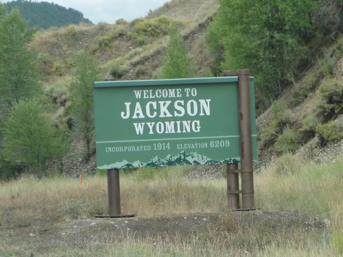 Sign welcoming visitors to Jackson, Wyoming, with details on incorporation and elevation, surrounded by greenery.