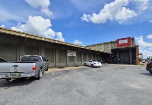 A parking lot with two cars in front of a large, industrial-style building under a partly cloudy sky.