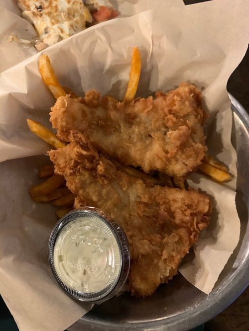 A basket containing two pieces of fried fish and a side of French fries, with a small cup of dipping sauce.