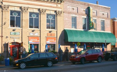 Historic brick buildings with colorful storefronts and outdoor seating, featuring Coca-Cola signage and parked cars.