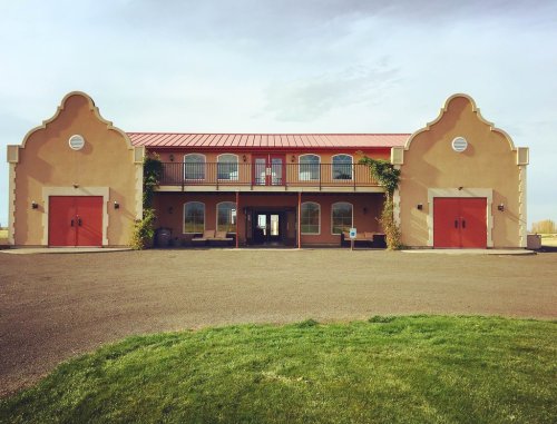 A two-story building with a red roof and orange doors, surrounded by green grass and a clear sky.
