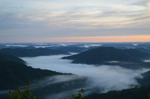 A serene landscape of rolling mountains shrouded in mist, with a soft sunrise illuminating the sky.