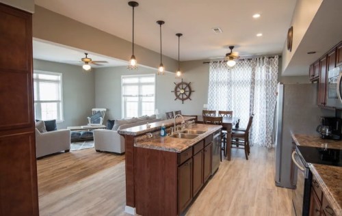 Modern kitchen with dark wood cabinets, island, and open layout to a cozy living area with light-colored furniture.