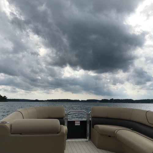 View from a boat with plush seating, overlooking a lake under a cloudy sky.