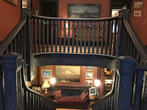 A view of a vintage staircase with dark wood railings, leading to a cozy sitting area adorned with paintings and lamps.