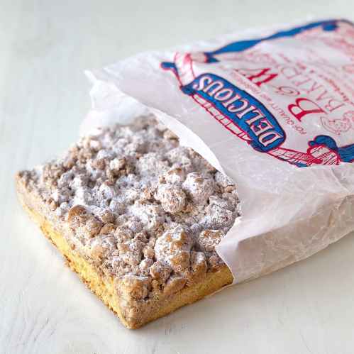 A partially open bag reveals a crumbly dessert topped with powdered sugar on a light surface.