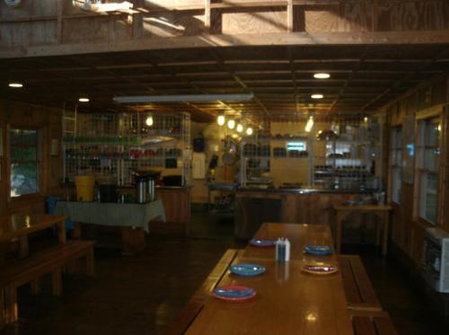 Interior of a rustic kitchen and dining area with wooden tables, colorful plates, and shelves filled with kitchenware.