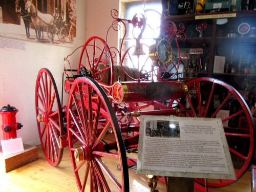 A vintage red fire engine displayed in a museum, with historical artifacts and a fire hydrant in the background.
