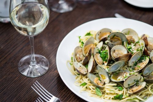 A plate of spaghetti with clams and herbs, accompanied by a glass of white wine on a wooden table.