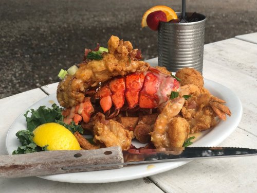 A plate of fried seafood, including lobster and shrimp, garnished with lemon and greens, alongside a cocktail.