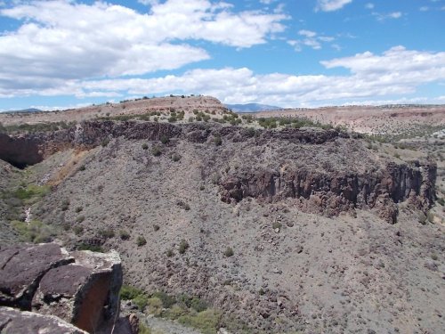 A rocky landscape with cliffs and sparse vegetation under a blue sky with scattered clouds.