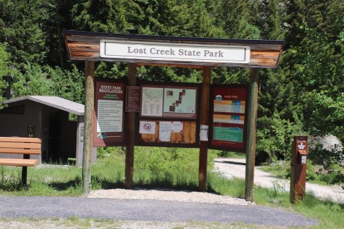 Sign at Lost Creek State Park displaying park regulations, fees, and information, surrounded by greenery.