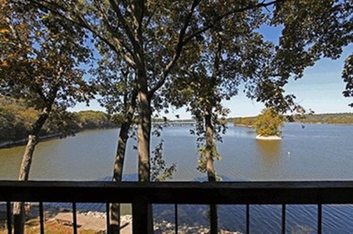 Scenic view of a river surrounded by trees, with a bridge visible in the distance under a clear blue sky.