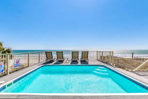 A clear blue pool overlooking a beach, with lounge chairs and a bright sky in the background.