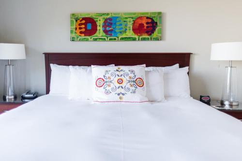 A neatly made bed with white linens, colorful decorative pillow, and modern lamps on bedside tables.