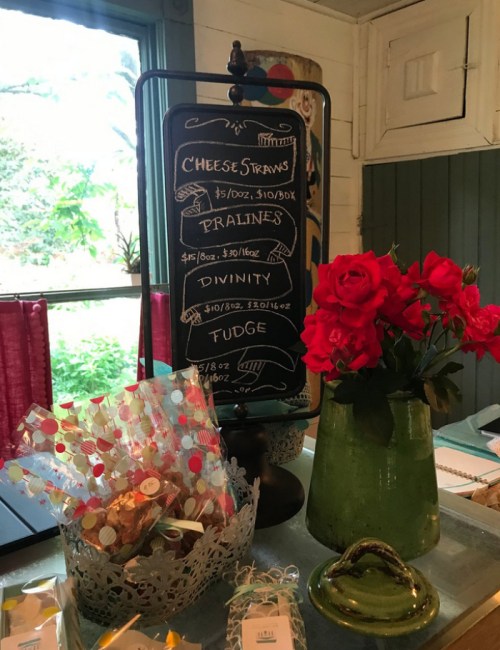 A chalkboard menu displays snacks like cheese straws, pralines, divinity, and fudge, with a vase of red roses nearby.