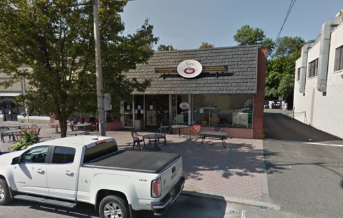 A small café with outdoor seating, surrounded by trees, and a white pickup truck parked in front.