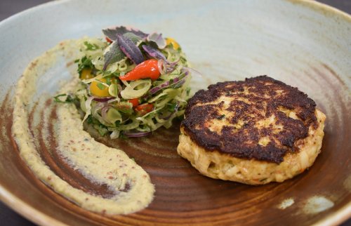 A plate featuring a golden crab cake, tangy mustard sauce, and a fresh salad with colorful vegetables.