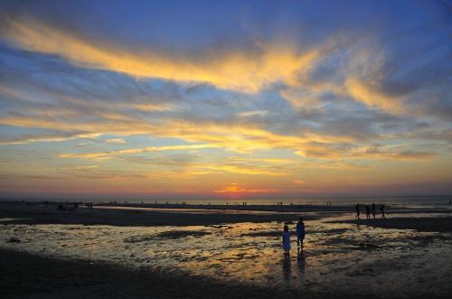 Silhouettes of people walking on a beach at sunset, with vibrant clouds and a colorful sky reflecting on the water.