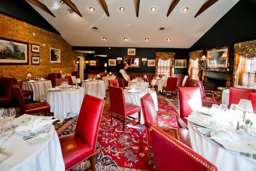 Elegant restaurant interior with red chairs, white tablecloths, and warm lighting, featuring a cozy atmosphere.