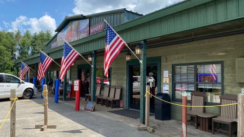 A green building with an open sign, featuring American flags and outdoor seating, set against a blue sky.