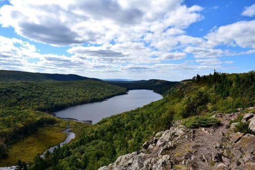 A scenic view of a river winding through lush green forests under a partly cloudy sky.