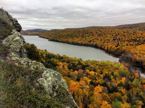 A scenic view of a river surrounded by vibrant autumn foliage and rolling hills under a cloudy sky.