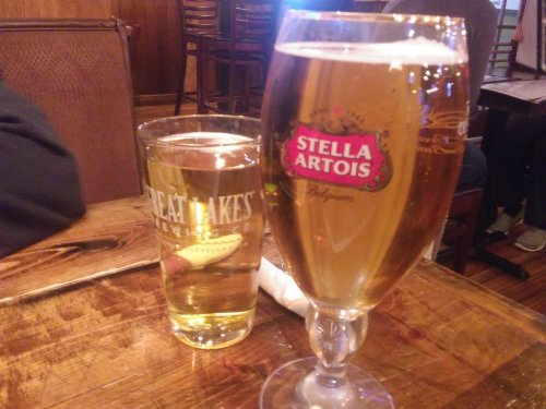 Two glasses of beer on a wooden table: a tall Stella Artois and a shorter Great Lakes Brewing glass.