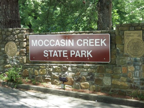 Sign for Moccasin Creek State Park mounted on a stone wall, surrounded by trees and greenery.