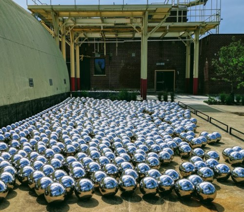 A large installation of shiny, reflective spheres scattered on a concrete surface near a building.