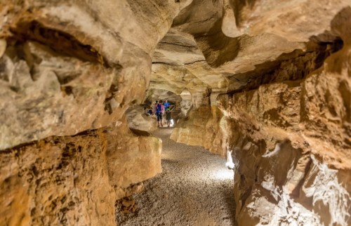 A dimly lit cave with rocky walls and a gravel path, featuring a few people exploring the underground space.