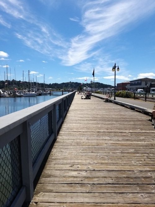 A wooden pier extends over calm water, with boats docked and a clear blue sky above.