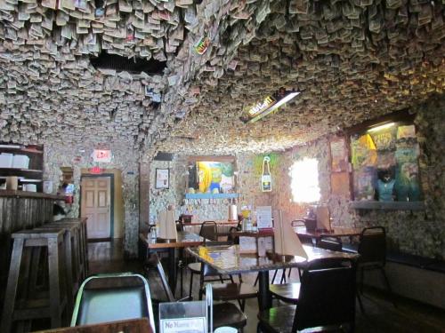 Interior of a quirky restaurant with walls and ceiling covered in dollar bills, featuring wooden tables and chairs.