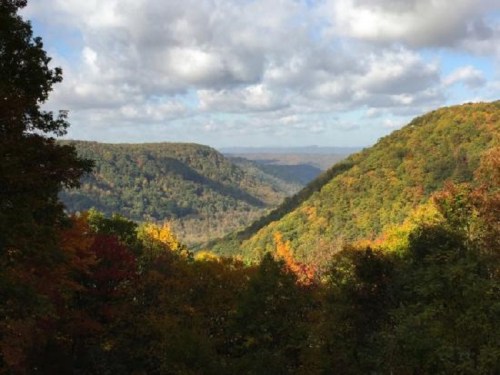 A scenic view of rolling hills covered in autumn foliage under a partly cloudy sky.