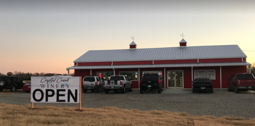 A red winery building at dusk with a large "OPEN" sign and parked cars in front.