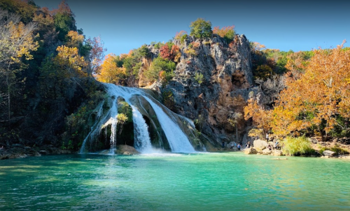 A serene waterfall cascades into a turquoise pool, surrounded by autumn foliage and rocky cliffs.