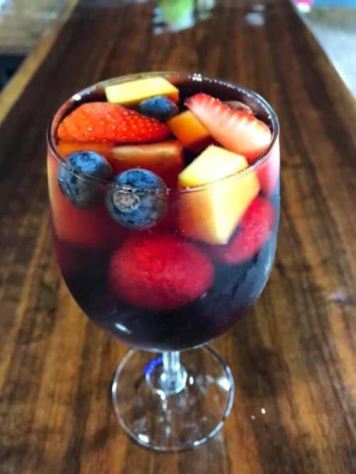 A glass of colorful fruit sangria with strawberries, blueberries, raspberries, and melon on a wooden table.