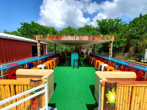 A vibrant outdoor tiki bar with colorful seating, a green carpet, and tropical decor under a blue sky.