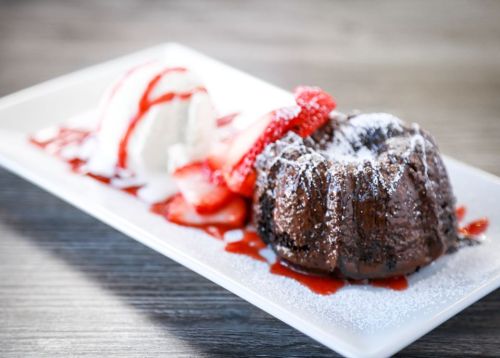 A chocolate lava cake topped with powdered sugar, served with vanilla ice cream and fresh strawberries drizzled with sauce.