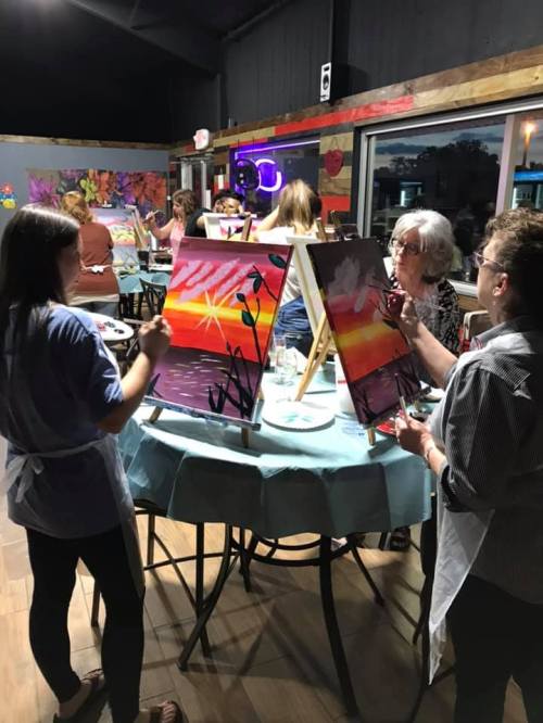 A group of people painting on easels in a vibrant art studio, with colorful canvases and a lively atmosphere.