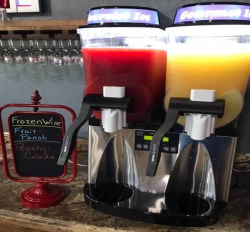 Two slushy machines with red fruit punch and yellow peach colada, next to a sign labeled "Frozen Wine."