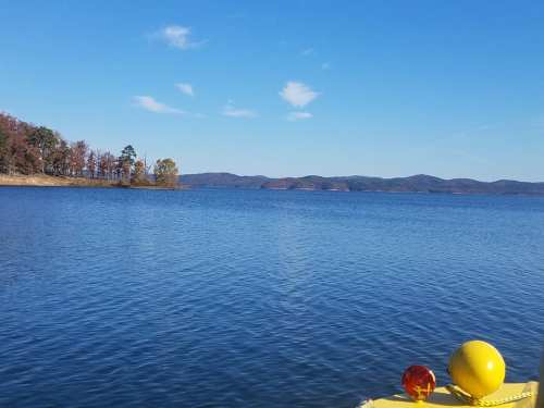 A serene lake view with mountains in the background and a clear blue sky, featuring colorful buoys in the foreground.