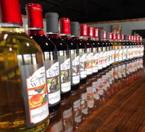A row of wine bottles with red caps on a polished wooden surface, showcasing various labels and colors.